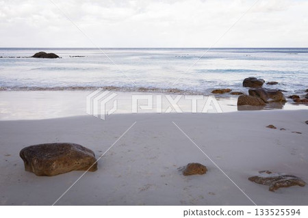 Flat design beach scene is showing pale sand with scattered boulders, calm sea under cloudy sky Flat design beach scene is showing pale sand with scattered boulders, calm sea under cloudy sky 133525594