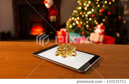Digital table on wooden table against Christmas tree Digital table on wooden table against Christmas tree 133525711