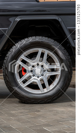 Close-up view of a shiny alloy wheel with red brake caliper on an SUV in a parking area Close-up view of a shiny alloy wheel with red brake caliper on an SUV in a parking area 133525793