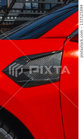 Close-up view of sleek red car showcasing unique carbon fiber details during daylight 133525894