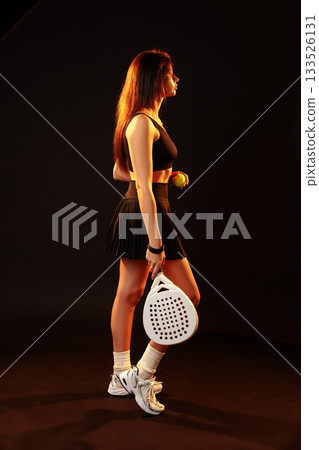 Young female athlete prepares for a tennis match in a studio setting with dramatic lighting 133526131