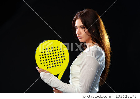 Female athlete prepares for a match with a bright yellow paddle in a dark setting Female athlete prepares for a match with a bright yellow paddle in a dark setting 133526175