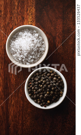 Salt and Pepper in Bowls on Dark Wood Surface, Top View 133526437