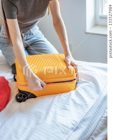 Woman packing suitcase on bed preparing for travel Woman packing suitcase on bed preparing for travel 133527984