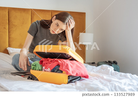 Woman feeling frustrated struggling packing clothes into luggage 133527989