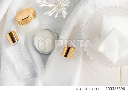 潔白的毛巾和保養品瓶整齊地擺放在磁磚地上。 潔白的毛巾和保養品瓶整齊地擺放在磁磚地上。 133528898