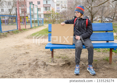 teenager sits on a blue bench with a box looking to the side teenager sits on a blue bench with a box looking to the side 133529274