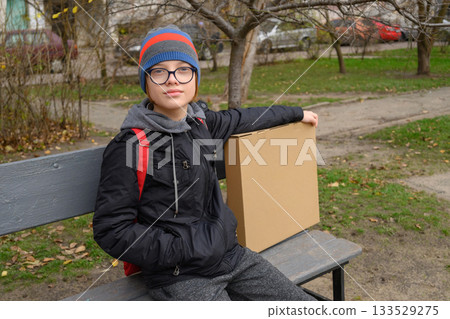 teenager sits on a grey bench with a box looking straight ahead teenager sits on a grey bench with a box looking straight ahead 133529275