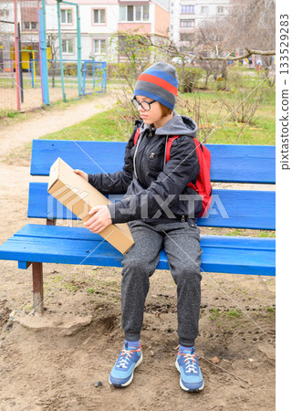 boy sits on a bench looking at a small box 133529283