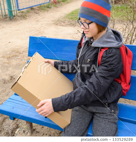 close-up of a boy sitting on a bench with a box 133529289