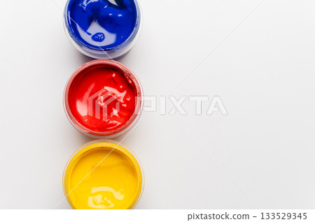 close-up shot of open small jars of gouache on a white background. A set of jars of gouache in different colors, viewed from above close-up shot of open small jars of gouache on a white background. A set of jars of gouache in different colors, viewed from above 133529345