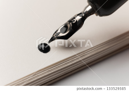 hand holds a smooth black pen in writing position against a clean white background where a drop of ink has just fallen. A contemporary ink drawing hand holds a smooth black pen in writing position against a clean white background where a drop of ink has just fallen. A contemporary ink drawing 133529385