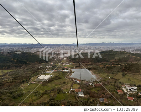 outskirts of Tirana, capital of Albania. View from ropeway Dajti Ekspres, buildings streets mountains valley cloudy sky winter 133529389