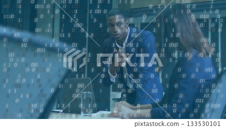 Gesturing businessman in dark blue suit leaning on conference table at office, with laptop and code Gesturing businessman in dark blue suit leaning on conference table at office, with laptop and code 133530101