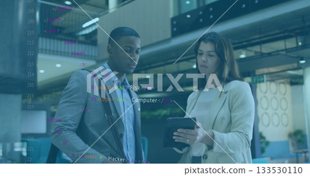 Reviewing code on tablet, professionals in blazers carrying shoulder bag in office atrium Reviewing code on tablet, professionals in blazers carrying shoulder bag in office atrium 133530110