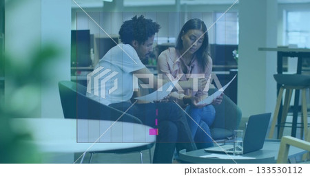 Reviewing printed documents, two professionals collaborating in office lounge chairs, with laptop Reviewing printed documents, two professionals collaborating in office lounge chairs, with laptop 133530112