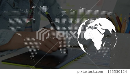 Holding stylus, artist drawing on tablet at desk, showing colored pencils and world map overlay 133530124