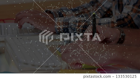 Two men in longsleeve shirts typing on keyboard and writing at office desk, charts and overlay Two men in longsleeve shirts typing on keyboard and writing at office desk, charts and overlay 133530125