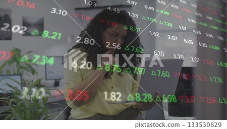 Analyzing stock market data, woman in mustard-yellow blouse focusing on laptop at office 133530829
