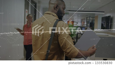Reviewing folder in office corridor wearing tan shirt watching colleague holding tablet, copy space 133530830