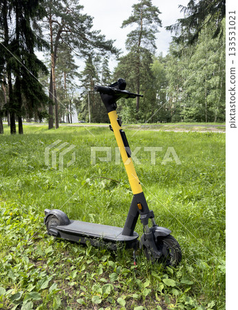 Electric scooter stands parked on grass. Modern urban mobility vehicle with battery powered wheel 133531021