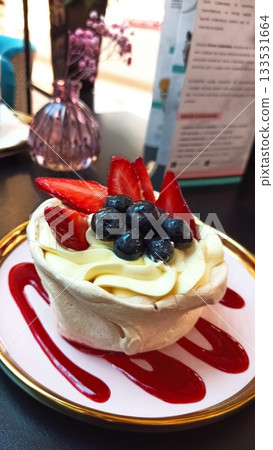 Delicate pavlova dessert topped with fresh strawberries and blueberries served with berry sauce. this image conveys sweetness, indulgence and elegant cafe enjoyment Delicate pavlova dessert topped with fresh strawberries and blueberries served with berry sauce. this image conveys sweetness, indulgence and elegant cafe enjoyment 133531664