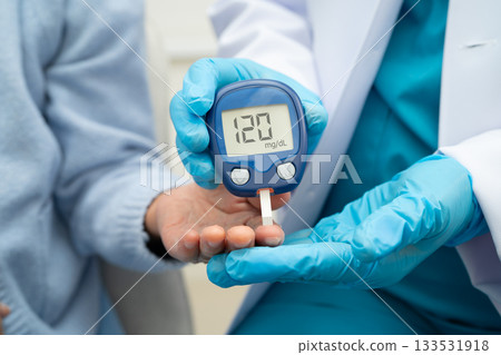 Asian doctor using digital glucose meter for check sample blood sugar level to treatment diabetes. 133531918