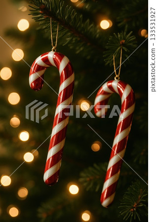 Candy cane ornaments hanging from a Christmas tree with warm glowing lights in the background. this image conveys festive cheer, holiday sweetness and cozy seasonal atmosphere 133531927