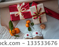 Top view of a red gift box with a beige gift box on top, both decorated with ribbons. A fresh tangerine lies on top, creating a warm and minimal festive composition suitable for Christmas, New Year 133533676