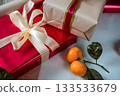Close-up view of a red gift box with a beige gift box on top, both decorated with ribbons. A fresh tangerine lies on top, creating a warm and festive composition suitable for Christmas, New Year 133533679