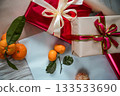 Medium view of a red gift box with a beige gift box on top, both decorated with ribbons. A fresh tangerine lies on top, creating a warm and festive composition suitable for Christmas, New Year 133533690
