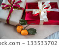 Medium view of two gift boxes, one red and one beige, placed side by side on a neutral background. A fresh tangerine lies nearby, creating a warm and festive holiday composition suitable for Christmas 133533702