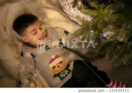Christmas coziness boy in sweater near tree enjoying holiday spirit and magic of childhood at home Christmas coziness boy in sweater near tree enjoying holiday spirit and magic of childhood at home 133534153