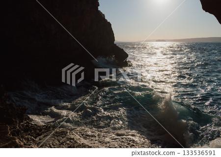 View from a cave to the sea on sunny day in summer. Mediterranean beauty landscape. Waves crashing on a rocky beach 133536591