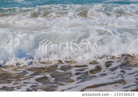 Moment when sea waves roll onto sandy beach creating white foam. Natural marine vacation background 133536815
