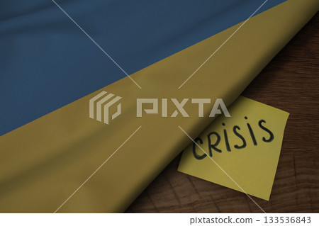 Fabric of the Ukraine flag on wooden surface and the word Crisis, concept of tense crisis situation in the country 133536843