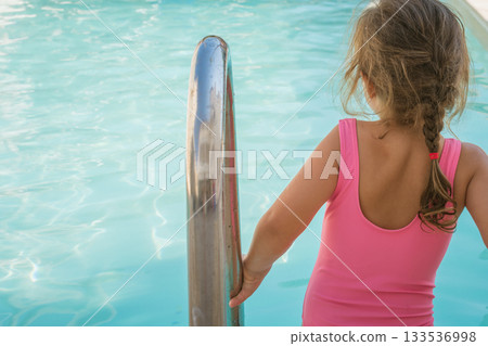 Little girl in swimsuit with a beautiful pool in the background 133536998