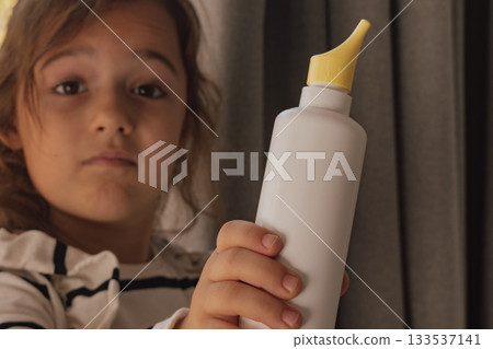 Cute girl holding an unbranded saline nasal spray bottle for children's health care 133537141