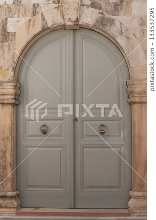 Old grey wooden double door with arched entry and massive ring handles, entrance to a historic building 133537295