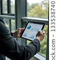 Business Professional Analyzing Data Charts on Tablet by Window in Modern Office Setting 133538740