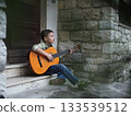 Young Boy Playing Guitar on Stone Steps Outdoors 133539512