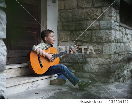 Young Boy Playing Guitar on Stone Steps Outdoors 133539512