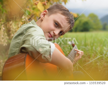 Young Boy Playing Guitar Outdoors in Nature 133539520