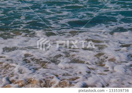 Moment when sea waves roll onto sandy beach creating white foam. Natural marine vacation background Moment when sea waves roll onto sandy beach creating white foam. Natural marine vacation background 133539736