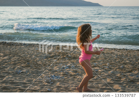 Little beautiful girl on the beach in a pink swimsuit eating pink heart-shaped ice cream 133539787