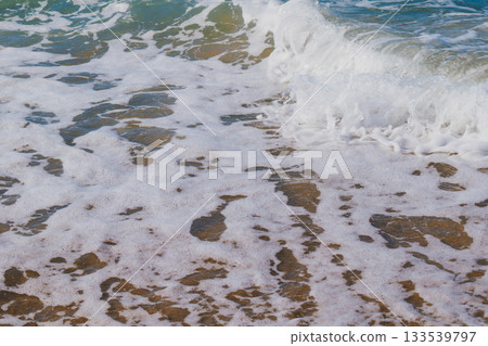 Moment when sea waves roll onto sandy beach creating white foam. Natural marine vacation background Moment when sea waves roll onto sandy beach creating white foam. Natural marine vacation background 133539797