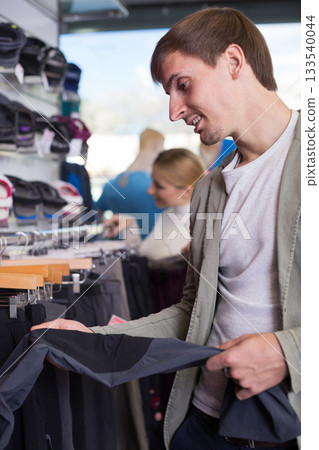 Customer examining pair of hiking trousers in sportswear store 133540044