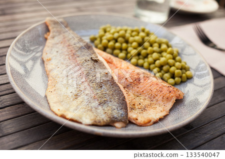 Fried trout fillets served with green peas 133540047