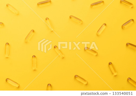 Top view of oil softgel capsules lie in rows diagonal on yellow background. Nutritional supplement contains fish oil, omega 3, omega 6, omega 9, vitamin e, vitamin d and vitamin a. 133540051