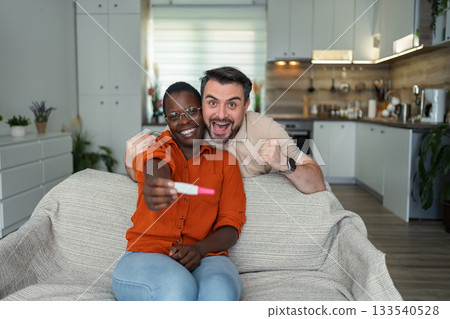 Excited multi-ethnic couple sharing pregnancy test result at home 133540528